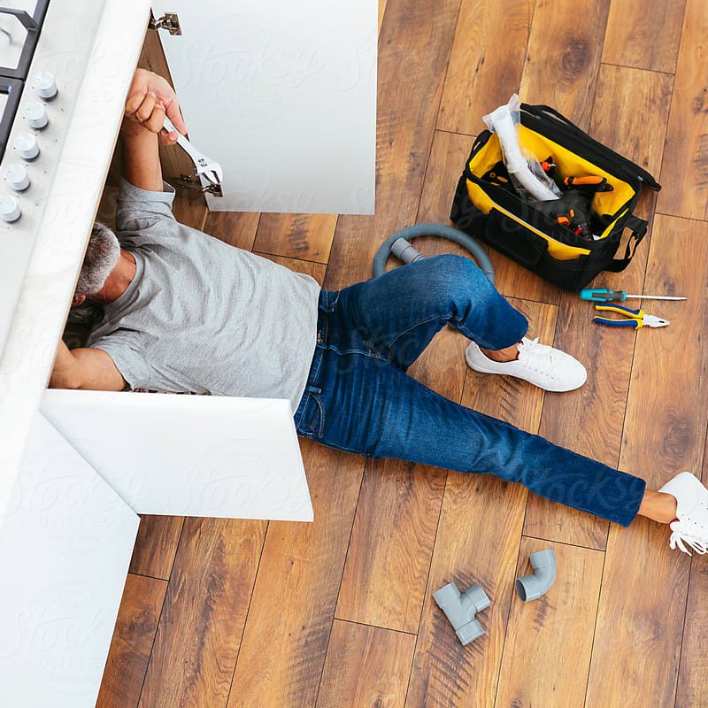 Greyish bearded man wearing casual clothes repairing broken kitchen stove of home with tools